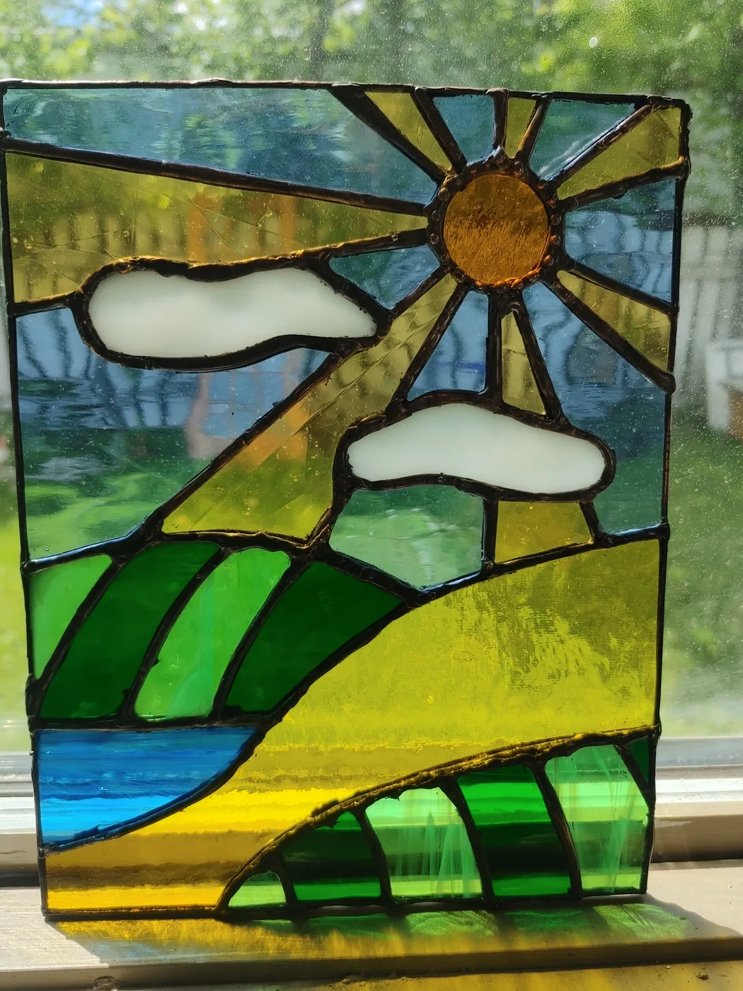Stained-glass prairie landscape with sun, clouds, and green hills