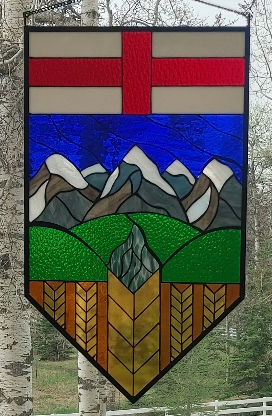 Alberta Crest stained-glass panel with red and white flag, blue sky, mountains, green foothills, and golden wheat